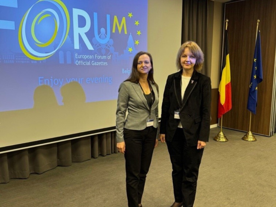 "Latvijas Vēstneša" valdes locekle un Oficiālo publikāciju departamenta tiesību aktu sistematizācijas vadītāja stāv pie ekrāna, uz kura rakstīts "European Forum of Official Gazettes"